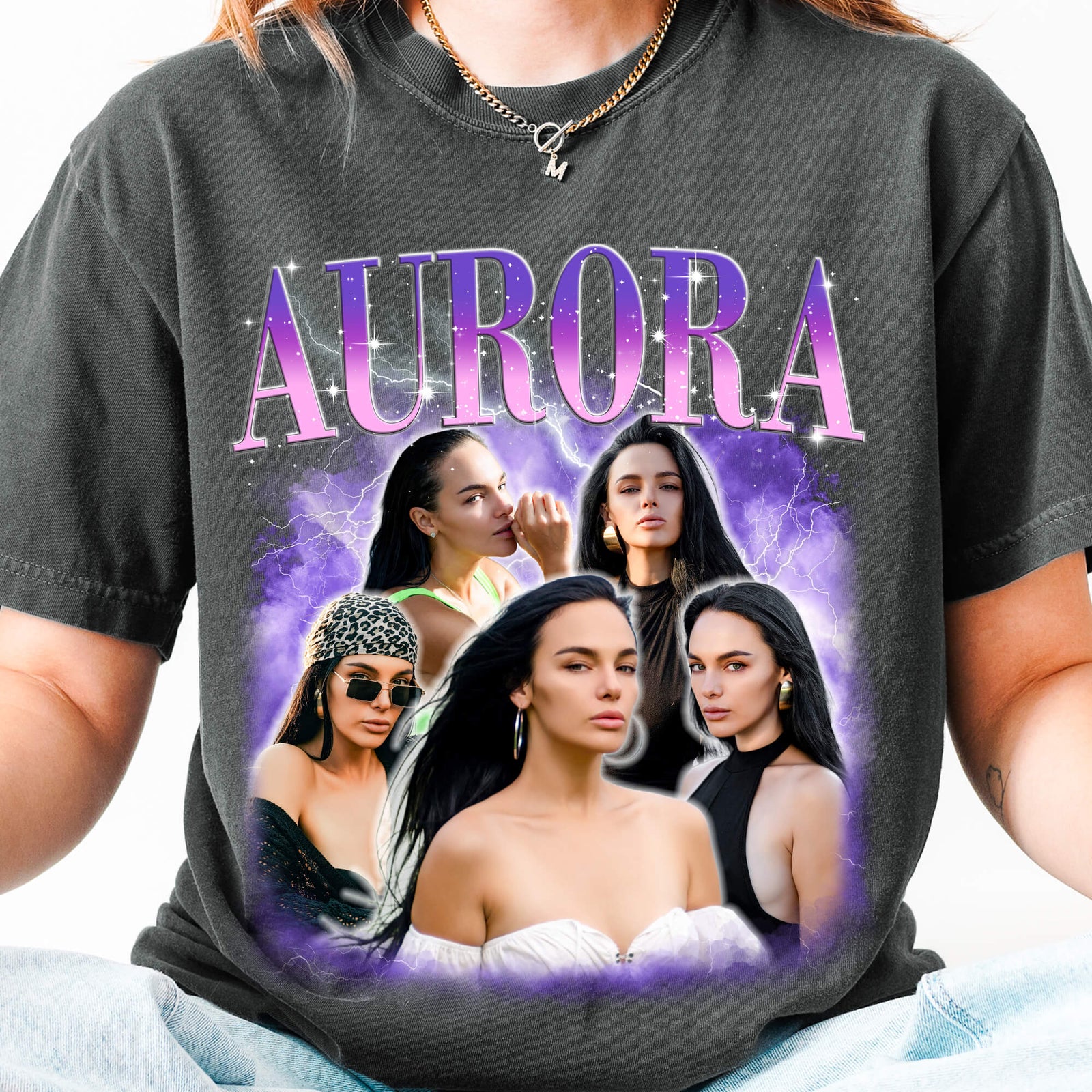 A person wearing a dark charcoal gray graphic t-shirt featuring the word 'AURORA' in purple gradient letters above a collage of five women with dark hair, set against a purple smoky background.