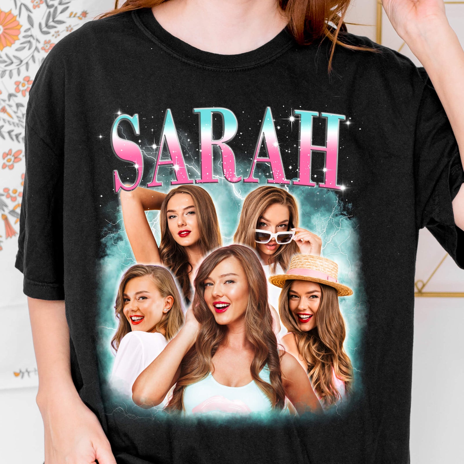 A black short-sleeve graphic T-shirt worn by a model, featuring the name 'SARAH' in pink and blue glitter-style letters above a collage of five photos of a woman with long brown hair.