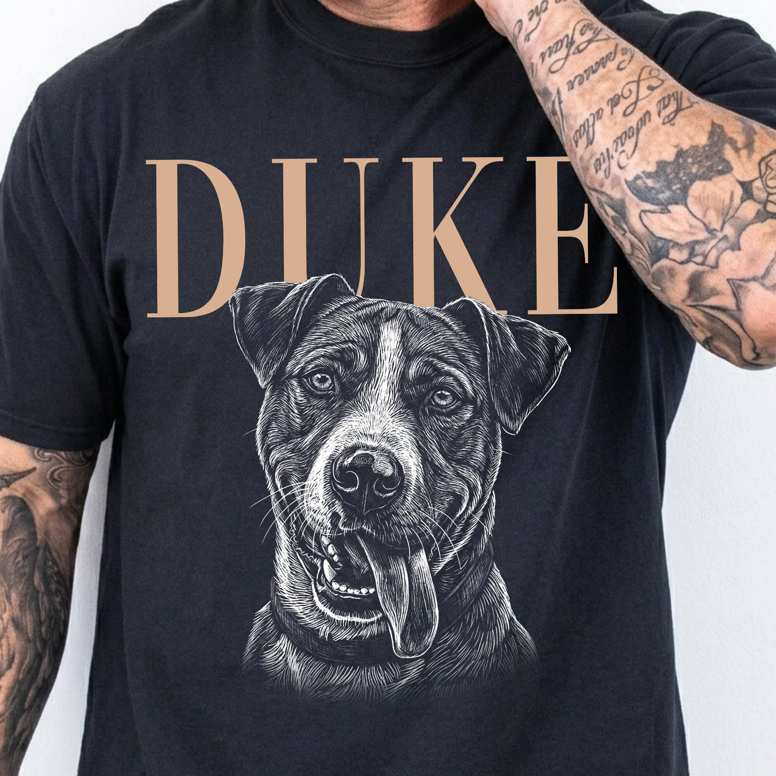 Man wearing a black T-shirt with the name DUKE in tan lettering above a large black-and-white portrait of a happy dog with its tongue out.